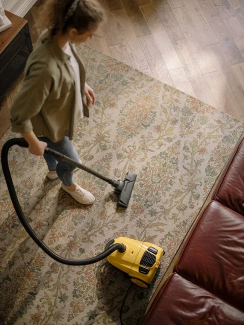 A hand in a glove using a vacuum to clean a car interior carpet, removing dirt effectively.